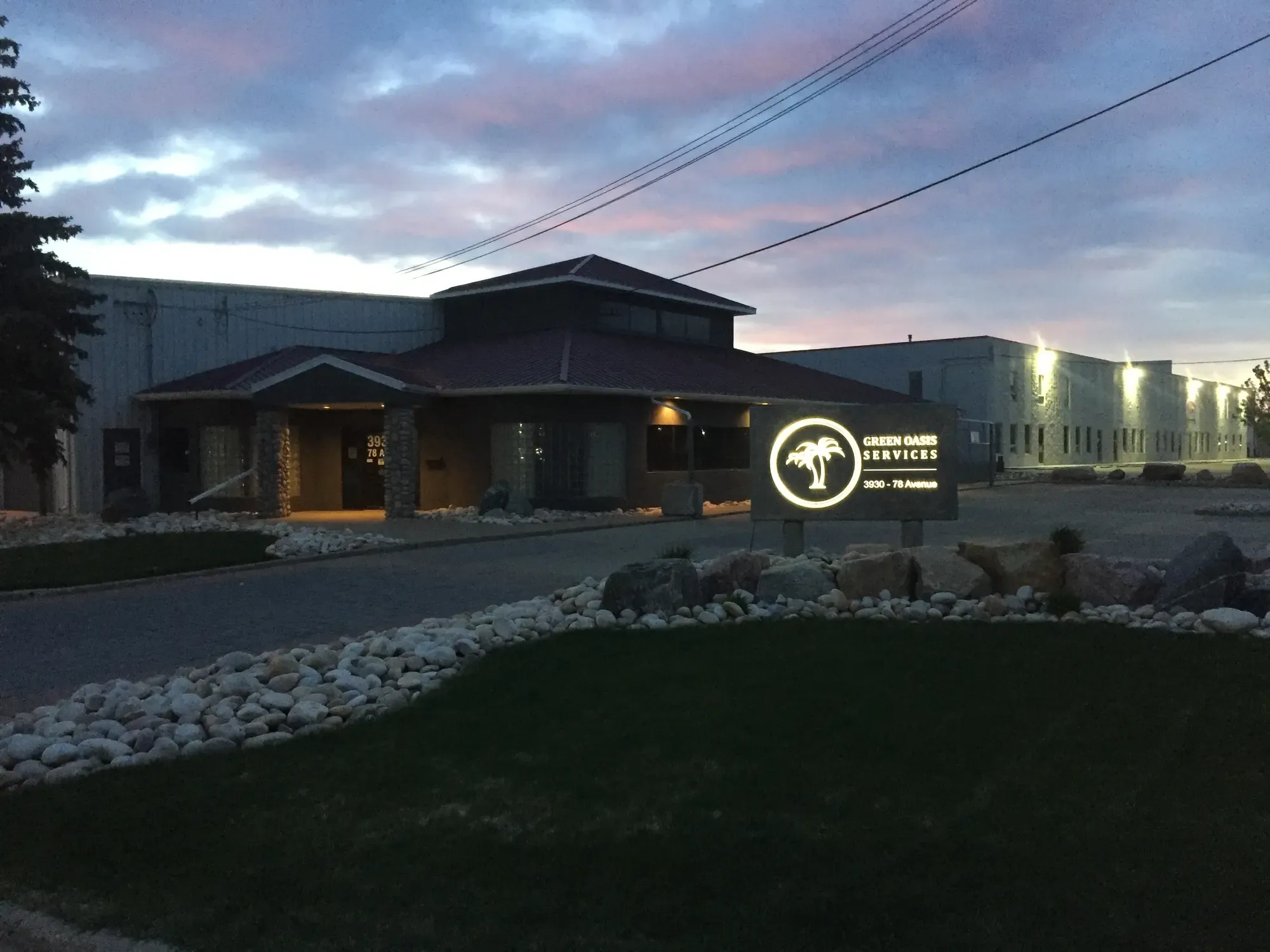 Green Oasis Services headquarters at dusk with illuminated sign